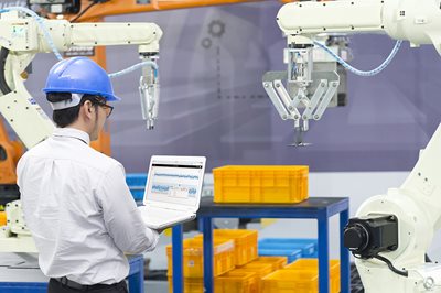 worker looking at laptop controlling robotic arm 